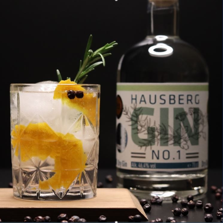 Ein Gin & Tonic als Serviervorschlag im Vordergrund mit einer Flasche Hausberg Gin No.1 rechts seitlich im Hintergrund.