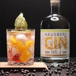 Ein Gin & Tonic mit Mandarinen als Serviervorschlag im Vordergrund mit einer Flasche Hausberg Gin No.2 rechts seitlich im Hintergrund.