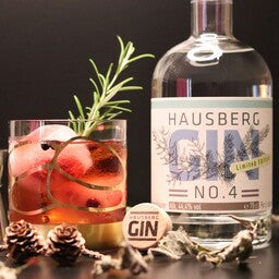 Ein Cocktail als Serviervorschlag im Vordergrund mit einer Flasche Hausberg Gin No.4 seitlich im Hintergrund.