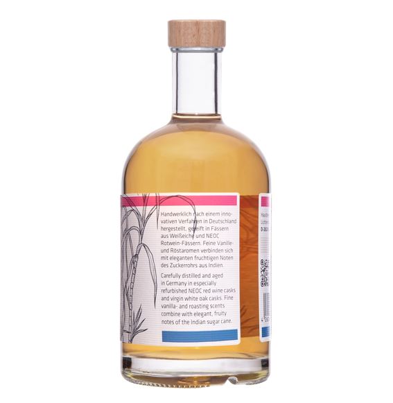 Eine Flasche Hausberg Rum Double Cask 3YO der Edition 3 mit weißem Etikett und Holzgriff-Verschluss in seitlicher Ansicht auf transparentem Hintergrund. Der Inhalt der Flasche erscheint gold-braun.

Auf dem Etikett ist ein Text mit Angaben zur Herstellung und Fasslagerung des Rums.
